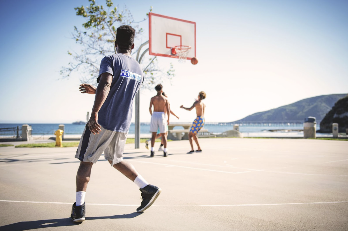 3 drenge spiller baskeball ved vandet i solen